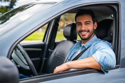 Portrait of a happy Latin American man driving his car and smiling at the camera through the window