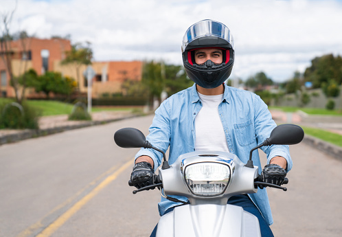 Portrait of a happy Latin American man riding a motorcycle and looking at the camera