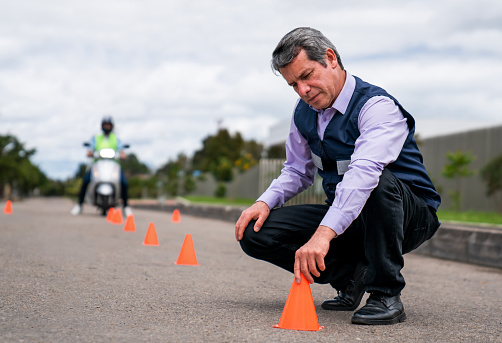 Motorcycle driving instructor putting traffic cones on the ground while teaching a lesson