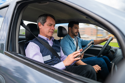 Driving instructor using a tablet while grading a man's driving test - learning to drive concepts