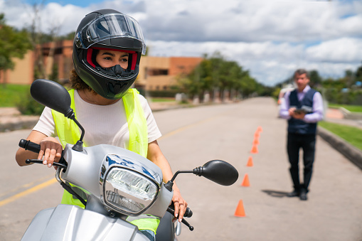 Latin American woman taking motorcycle driving lessons and instructor watching her - learning to drive concepts