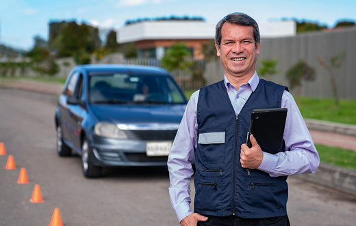 Portrait of a happy Latin American driving instructor in front of a car and looking at the camera smiling