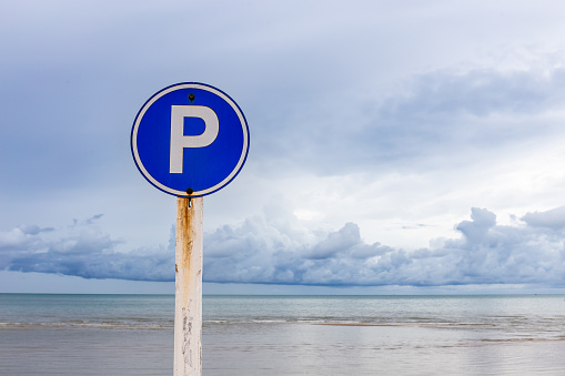 Beach parking sign with sky and sea as background.