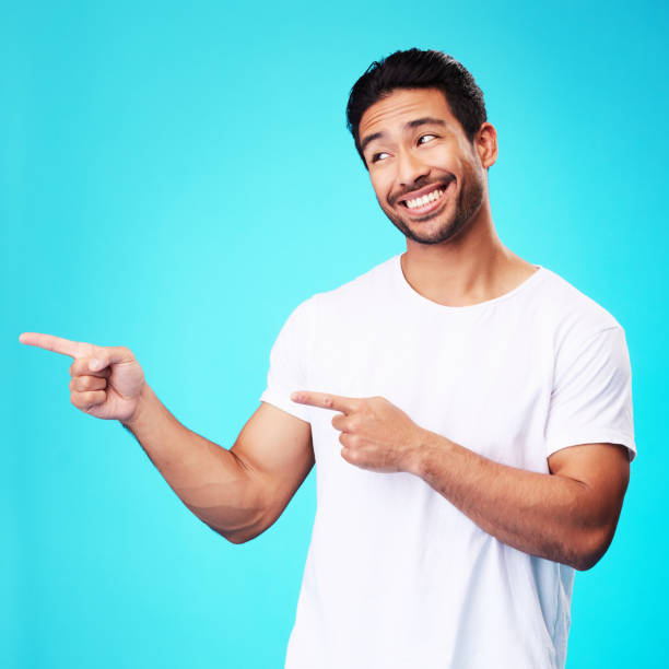 istock Mockup, pointing and man with a smile, thinking and choice against a blue studio background. Male person, decision or model with product placement, hand gesture and presentation with sign and showing 1582812110
