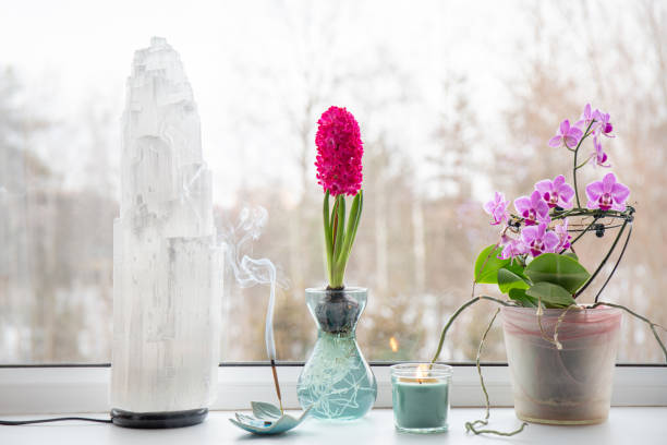 istock Home window sill with various spiritual objects. Big electrical gemstone selenite lamp, incense candle burning, candle, orchid flower pot. 1582822894