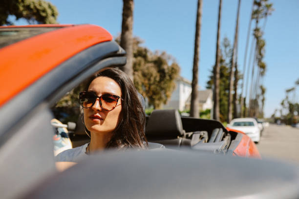 Woman driving a convertible car on a sunny day in Santa Monica, California relaxing, enjoying her day.