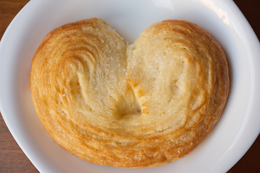 A bun in the shape of a heart. Top view. A bun isolated on a white background. Fresh bun with sugar. Delicious dessert. Confectionery product.