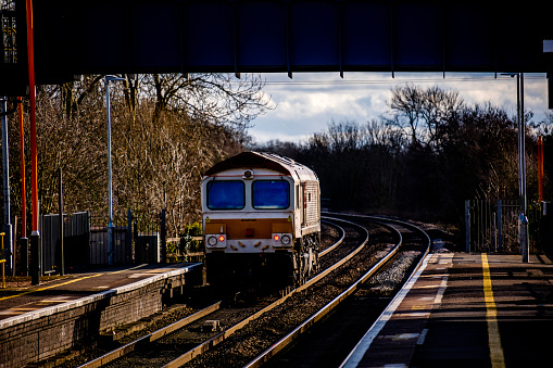 A station England UK. Diesel powered railway line in the English countryside. Station on a sunny day. Freight Train with wagons.