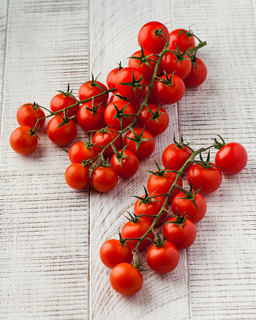 Ripe juicy cherry tomatoes on a branch on a white wooden background. The concept of vegetables.