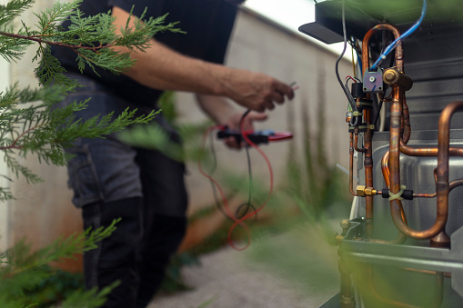 An unrecognizable technician installs a heat pump in the courtyard of a residential building