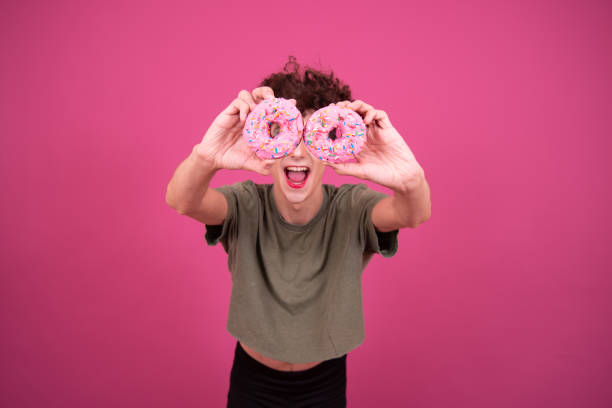 istock Funny drag queen poses in the studio on a pink background and eats donuts. 1582937997