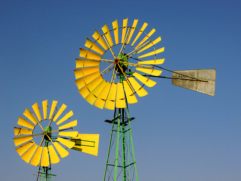 Cheerful yellow and green painted windmills against a blue sky.