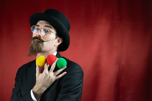 Vintage Caucasian Magician with top hat, glasses and mustache with colored balls with red background