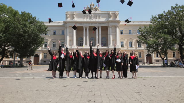 A group of cheerful students in graduation robes throws up their square academic caps as a symbol of university graduation