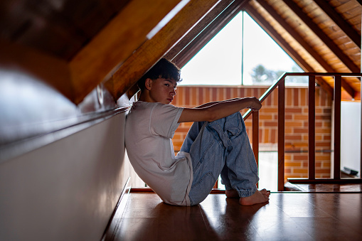 The young teenager is lying on the loft floor, his eyes reflect a mixture of fear, uncertainty and sadness, as if he is dealing with difficult thoughts and situations, indicating anxiety and nervousness. The palms of his hands may be sweaty, showing the intensity of his emotions.