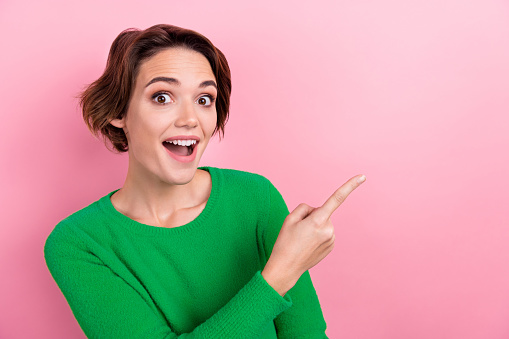 Photo of excited funky lady wear green pullover pointing finger empty space isolated pink color background.