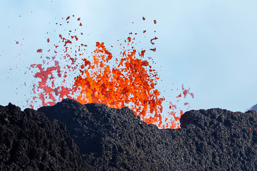 Close up shot of lava ejection from a volcanic crater. The edge of the new crater of black lava and the orange magma / melted lava is seen. The sky in the background. Volcano eruption in Iceland, Reykjanes, Litli-Hrutur.