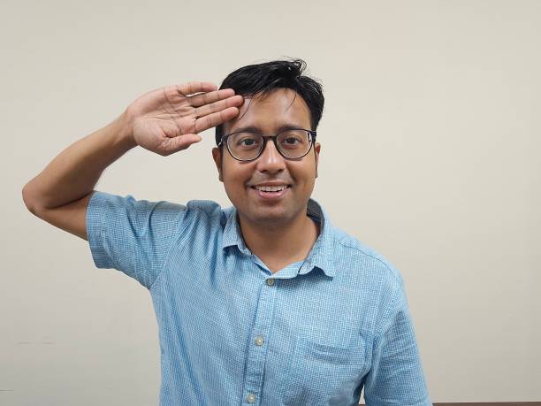 Indian man with glasses in a blue shirt showing salute pose against a gray background An Indian man with glasses in a blue shirt showing salute pose against a gray background honorably stock pictures, royalty-free photos & images