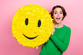 Photo of astonished overjoyed lady blogger wear green stylish clothes hand hold big yellow emoticon isolated on pink color background