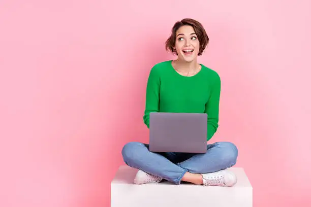 Full length photo of shiny excited lady wear green pullover working gadget looking empty space isolated pink color background.