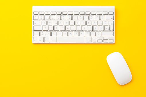 Computer keyboard and mouse on yellow background. Copy space