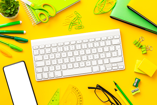 Computer keyboard and office supplies on yellow background