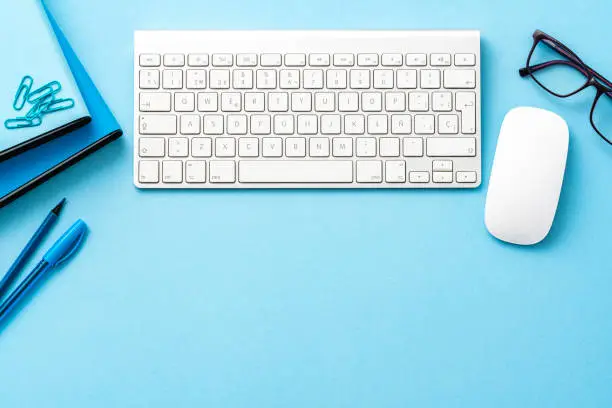 Photo of Blue colored office desk: computer keyboard and mouse and office accesories with copy space.