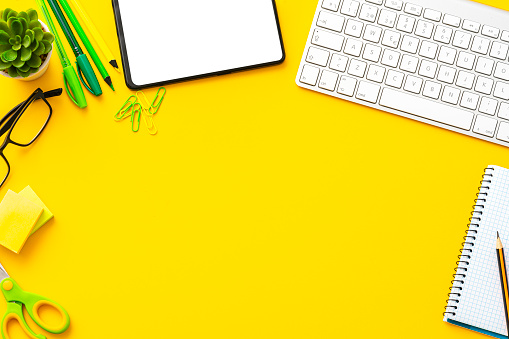 Yellow colored workspace: keyboard, digital tablet and office supplies with copy space.