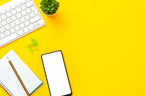 istock Yellow colored office desk: keyboard, mobile phone note pad  with copy space. 1583048031