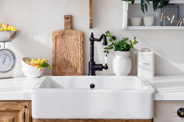 black faucet in vintage style and ceramic sink at kitchen detail in kitchen interior. black faucet in vintage style, ceramic sink, cutting board, bowl with grape, parsley in jug and metal food container on white countertop vintage kitchen scale with fruit stock pictures, royalty-free photos & images
