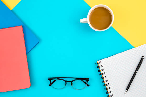 istock Notebook, eye glasses and cup of coffee on a blue and yellow background. 1583055852