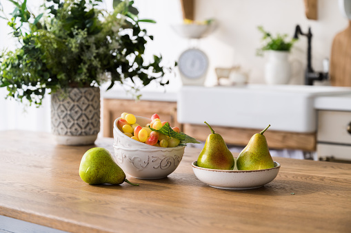 selective focus on ripe pears on plate, grape in ceramic bowl and flowers in vase on wooden dining table on home kitchen background. fresh fruits on tabletop. healthy eating concept.