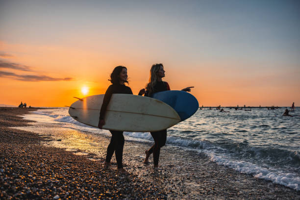 Two Young Female Surfers Having A Conversation Before A Sunrise Surf Session In Barcelona