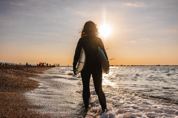 istock Female Surfer Carrying Two Surfboards At The Beach 1583064349