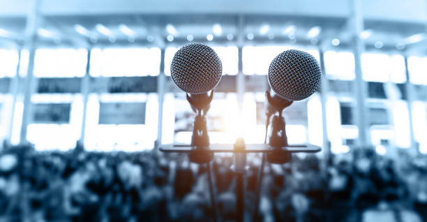 Closeup microphone in auditorium with blurred people in the background Closeup microphone in auditorium with blurred people in the background press room stock pictures, royalty-free photos & images