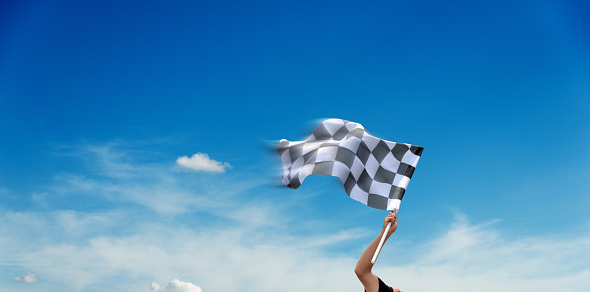 Checkered race flag in hand against blue sky