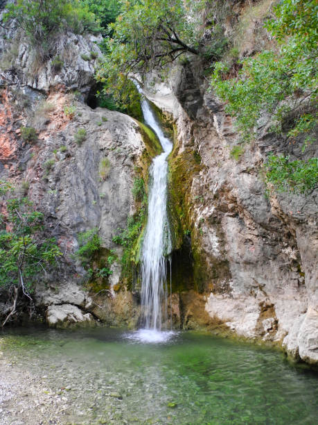 istock Mountain waterfall falling from picturesque rocks into emerald lagoon with pebble beach 1583088591