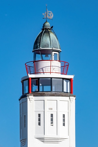 An old lighthouse featuring a metal roof with a weathervane perched atop, standing tall on a rocky shoreline