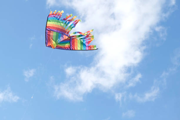 Kite in a blue sky. Rainbow Delta Kite flying among the clouds. Happy growing years moment. Outdoor time spending. Aspirations, target, inspiration concept. Freedom and summer holiday. Childhood dream cometa en un cielo azul. rainbow delta kite volando entre las nubes. feliz momento de los años de crecimiento. gasto de tiempo al aire libre. aspiraciones, objetivo, concepto de inspiración. libertad y vacaciones de verano. sueño de la infancia
