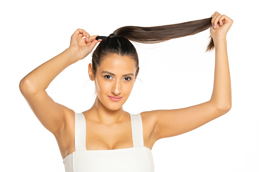 Young smiling woman adjusting her hair in a ponytail on a white background