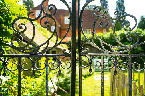 Shallow focus of an ornate wrought iron gate leading to a private garden. A large house can be seen in the distance.