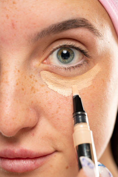 istock Young woman applyes concealer under her eyes 1583171333