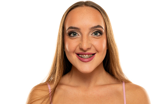 portrait of a young beautiful smiling woman with makeup and braces on a white background