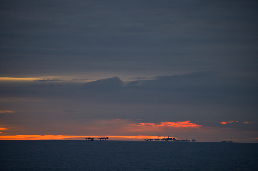 Distant oil/gas rigs silhouetted against a setting sun in the North Sea off the coast of England
