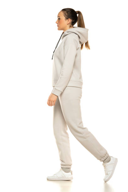 a young woman in a gray tracksuit and pony tail wakling to a white background in the studio stock photo