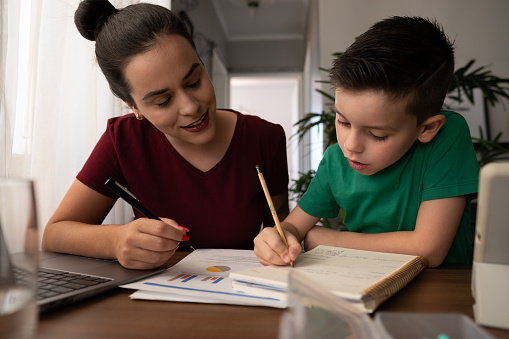 Young son studies and does homework with help of mother in home room