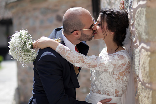 A young bridal couple kisses beside a stone wall
