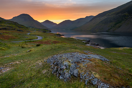 A fiery orange sunrise taken on a Summer morning at Wastwater in The English Lake District. The photograph was taken near the lakeshore of this beautiful Cumbrian landscape with a view of Yewbarrow, Great Gable and Scafell Pike in the background.