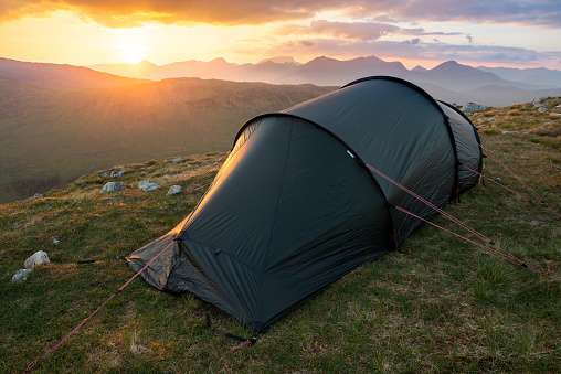 Wild camping in Glencoe. Tent pitched in remote wilderness landscape with sunset in background setting behind mountains of the Scottish Highlands.