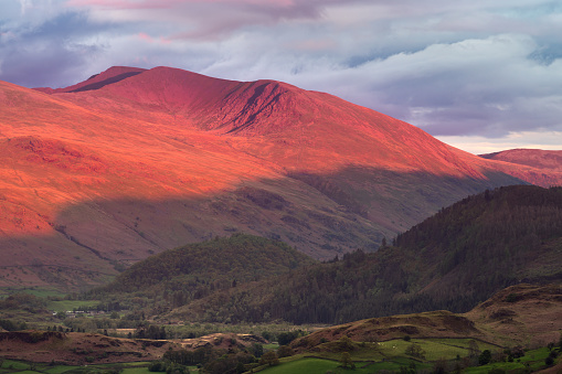 Evening light from the sunset casting a red glow and long shadows on Helvellyn mountain range in the English Lake District.